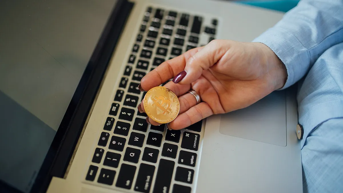 Physical Bitcoin coin held next to a laptop